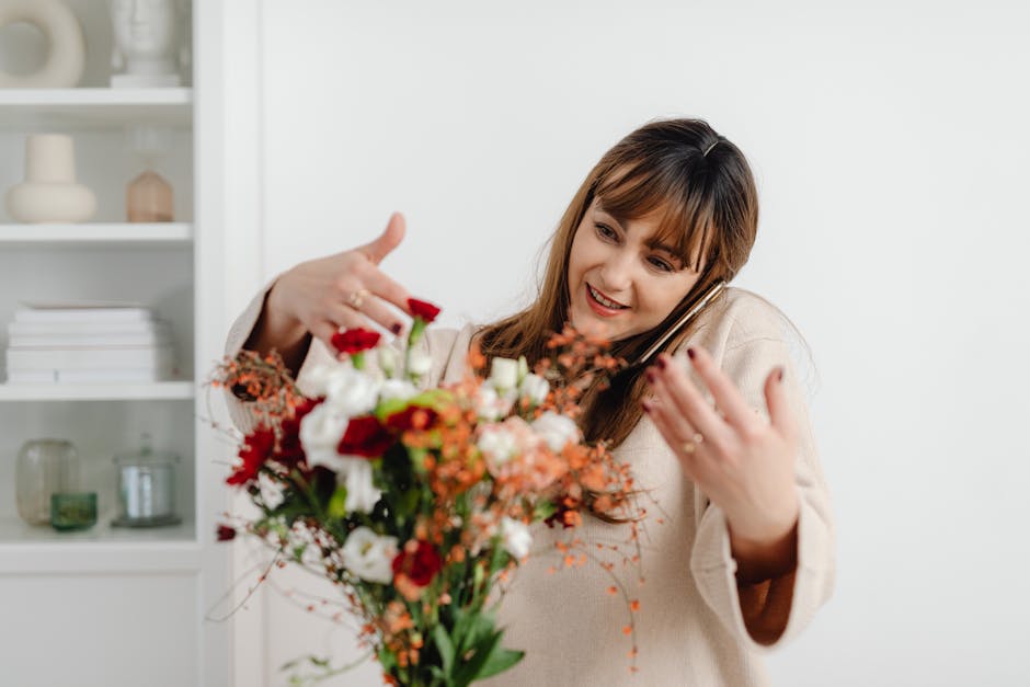 A woman with shoulder-length brown hair and a warm smile is holding a vibrant floral bouquet in one hand while talking on her mobile phone with the other. The bouquet features a variety of fresh flowe