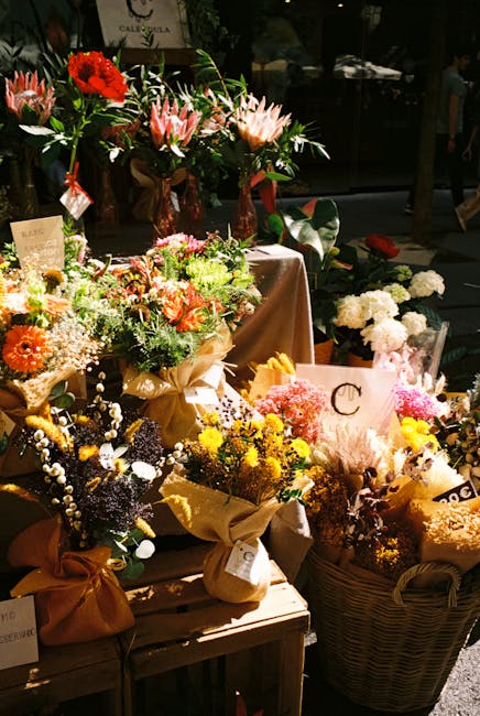 A display of vibrant floral arrangements and bouquets arranged on a wooden table at a flower shop. The collection includes various types of fresh flowers such as pink and white lilies, bright yellow,